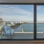 Blick auf Wasser und Ufer mit Liegeplatz vor großem Fenster.