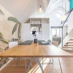 Esszimmer mit Holztisch, Stühlen und Palmenwand. Hintergrund: Küche und Treppe.