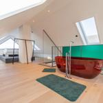 Dachgeschosszimmer mit roter Badewanne und Bett unter Dachschrägen.