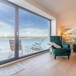 Wohnzimmer mit Meerblick, grüner Sessel und Balkon mit Liegestühlen.