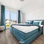 Schlafzimmer mit blauem Bett, Fensterblick und Holzboden.