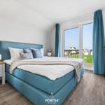 Schlafzimmer mit blauem Bett, großem Fenster und Holzboden.