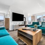 Wohnzimmer mit türkisfarbenen Sofas, Holzfußboden und Fernseher an der Wand.