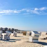 Strand mit Strandkörben und Holzsteg unter blauem Himmel.