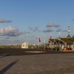 Strandpromenade mit rotem Gebäude und Fahnen unter blauem Himmel.