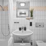 Badezimmer mit Dusche, Waschbecken und Toilette. Weiße Fliesen mit floraler Bordüre.