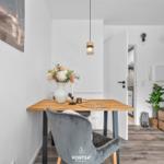 Essbereich mit Holztisch, grauer Stuhl und Blumenvase. Hintergrund: Küche und Kleiderschrank.