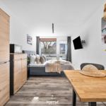 Schlafzimmer mit Bett, TV und Essbereich. Holzfußboden und Fenster zum Balkon.