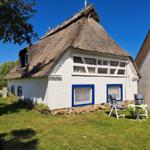 A white house with thatched roof, blue window frames, and garden furniture in the front yard.