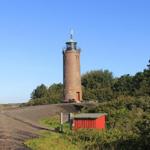 Roter Leuchtturm auf grüner Anhöhe mit Wald und Weg