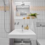Badezimmer mit Dusche, Waschbecken und Toilette. Weiße Fliesen mit floraler Bordüre.