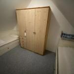 Zimmer mit Schlafcouch, Kleiderschrank und Kinderbett unter Dachschrägen.