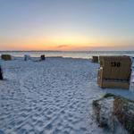 Strand mit Liegestühlen und Sonnenuntergang am Horizont.
