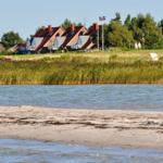 Strand mit Wasser, Grasland und Häusern im Hintergrund.
