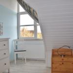 Schlafzimmer mit Bett, Nachttisch, Stuhl und Schrank. Fenster mit Blick nach draußen.