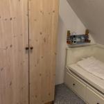 Kleines Schlafzimmer mit Dachschrägen, weißem Bett und Holzschrank.