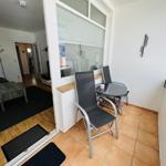 Balcony with table and chairs, view into living room with sofa and coffee table.