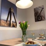 Dining table with pasta, wine, and flowers. Wall art shows beach and bike.