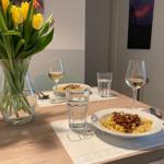 Table with pasta, wine, and tulips in dining area.