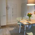 Dining table with chairs, flowers, and pendant light in a room with wooden floor and white walls.