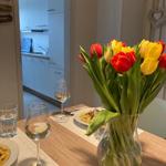 Dining table with flowers, glasses, and food. Kitchen in background.