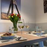 Dining table with pasta, wine, and tulips. Wall art shows bicycle and wooden structure.