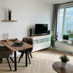 Wohn- und Essbereich mit TV, Tisch und Stühlen. Blick aufs Meer durch große Fenster.