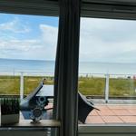 Blick auf das Meer von einer Terrasse mit Liegestühlen und Glasgeländer.