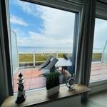 Terrasse mit Tisch und Stühlen bietet Meerblick. Fenster mit Vorhängen und Dekoration.