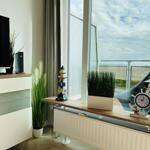 Wohnzimmer mit TV, Pflanzen und Meerblick durch große Fenster.