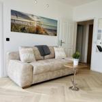 Wohnzimmer mit Sofa, Wandbild und Holzboden. Blick in Schlafzimmer und Bad.