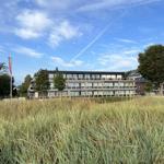 Moderne mehrstöckige Villa mit Balkonen und Glasfassade. Vordergrund: hohes Gras und Bäume.