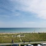 Strand mit grüner Dünenflanke und Wanderweg. Menschen genießen die Küstenlandschaft.