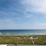Meer und Strand mit Grünflächen und Besuchern unter blauem Himmel.