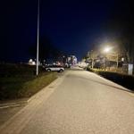 Nachtansicht einer Straße mit Beleuchtung, Bäumen und geparkten Autos.