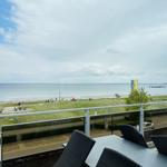 Terrasse mit Tisch und Stühlen bietet Blick auf Strand und Meer.