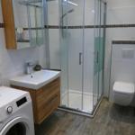 Badezimmer mit Dusche, Waschbecken und Toilette. Waschmaschine und Spiegel sind vorhanden.