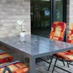 Terrasse mit Glas-tisch und Stühlen mit bunten Kissen.