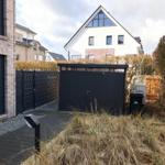 Hinterhof mit schwarzer Garage und Zaun, umgeben von Sträuchern und Gras.