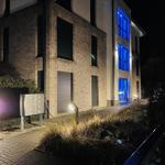 Moderne Hausfassade bei Nacht mit blau beleuchteten Fenstern und gepflastertem Weg.