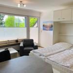 Schlafzimmer mit Doppelbett, Sitzgelegenheit und Fensterblick auf Grün.