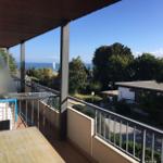 Terrasse mit Tisch und Stühlen, Blick auf Meer und Bäume.