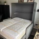 Bedroom with fold-down bed, wall shelf, and pictures on the wall.