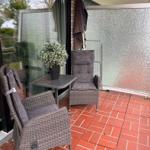 Terrace with two chairs, table, and plant. Red tiled floor and glass wall.