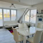 Wohn- und Essbereich mit weißem Sofa, Tisch und Stühlen sowie großen Fenstern.