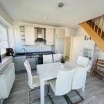 Küche und Essbereich mit weißem Tisch, Stühlen und Holztreppe.