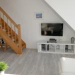 Wohnzimmer mit Holztreppe, Fernseher und weißem Sofa.