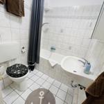 Badezimmer mit Badewanne, Toilette und Waschbecken. Boden- und Wandfliesen. Anker-Matte.