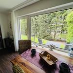 Essbereich mit Tisch, Stühlen und Blick auf Garten. Küchenbereich im Hintergrund.
