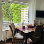 Esstisch mit vier Stühlen vor großem Fenster mit Blick auf Garten.